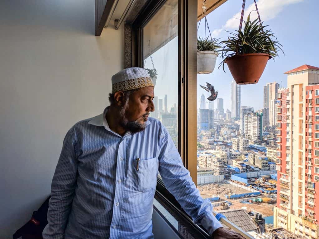 Man stands in the window of his newly redeveloped house with a view of the cityscape.
