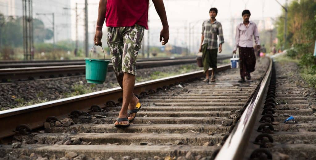 Boys walking along railway tracks with a bucket of water