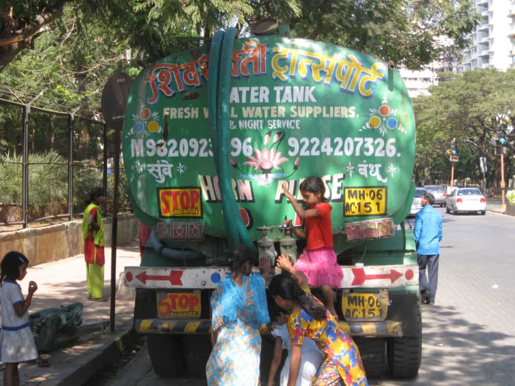 A family fills water from a tanker truck in Mumbai. Children help.