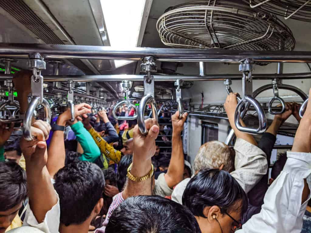 a group of people hold onto railings in a moving local train in Mumbai