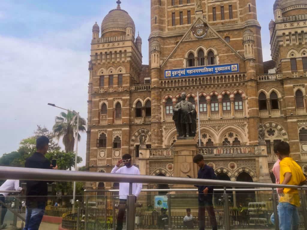 People posing for pictures in front of the BMC building, with Pherozeshah Mehta's statue in the background