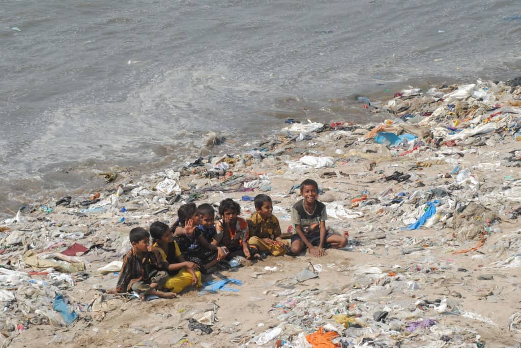 children sit on a pile of waste on Versova beach in Mumbai