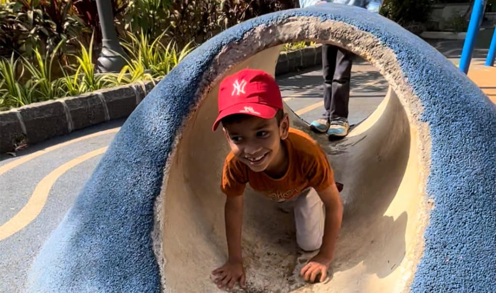 A child coming out of a tunnel in a park smiling