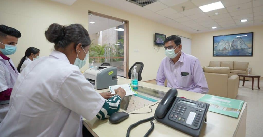 a masked patient at a COVID hospital in mumbai sits with a receptionist for enquiries