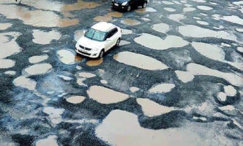 Cars drive over pothole-filled tar road in Mumbai
