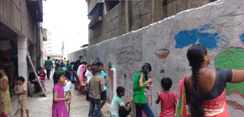 Women and children painting the wall next to a building with art