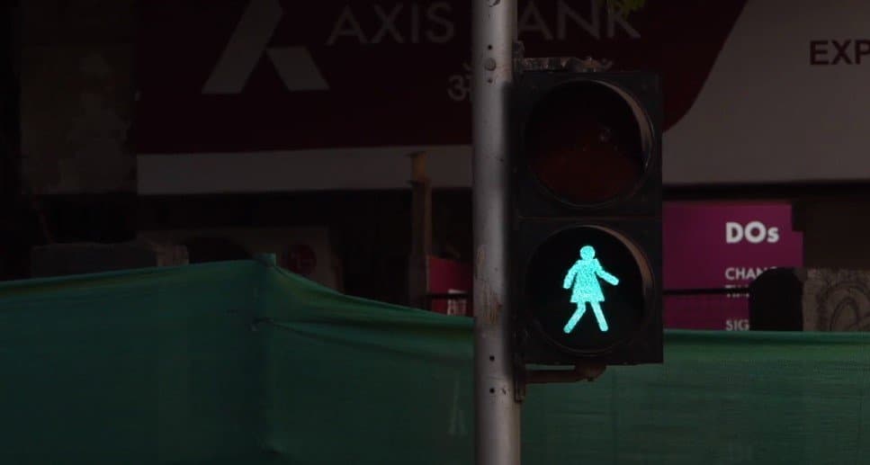 A green stick figure woman on a traffic light signifying it's okay to walk, unlike the generic man