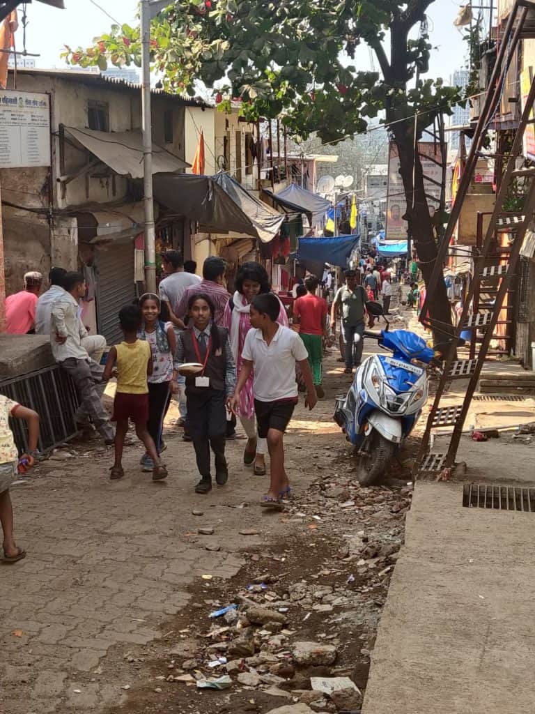 People and kids in school uniform walking in a lane in an informal settlement