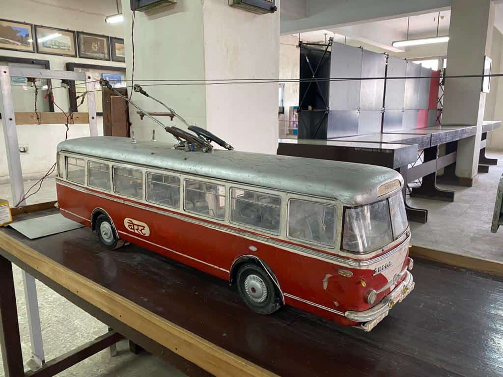 table top model of a red Skoda bus with tires below and overhead electric wires