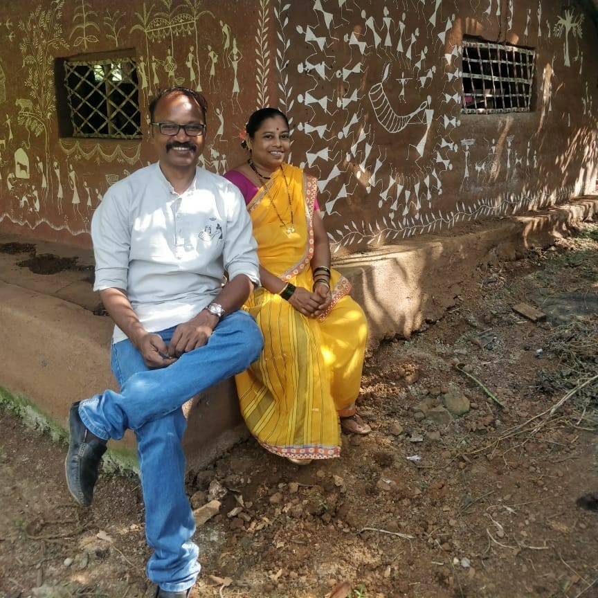 Prakash and Pramila Bhoir are sitting outside their house which is covered with Warli art. 
