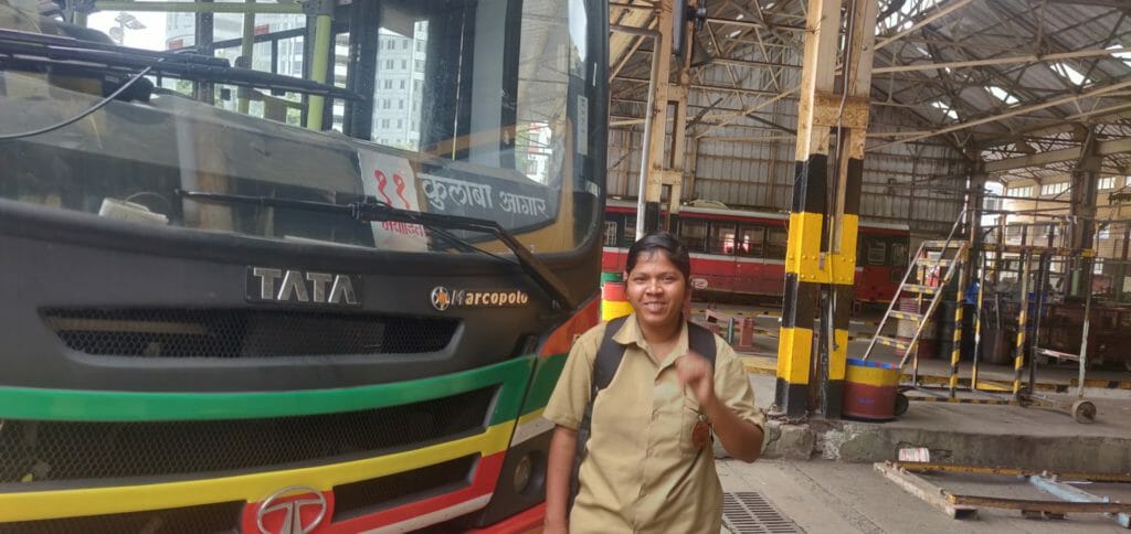 Bano Abdul Sattar smiling for the camera, standing beside the 11 number bus that she drives. She is wearing her driver's uniform.