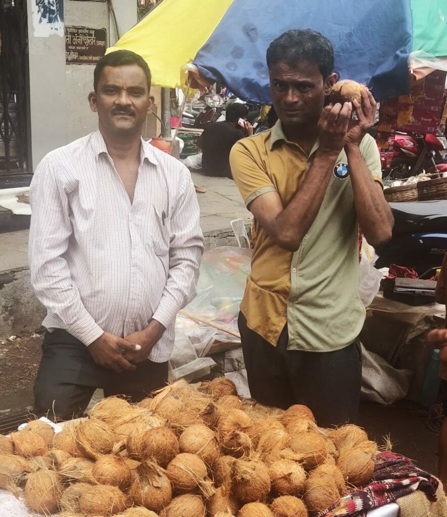 A coconut seller poses for the camera as his customer stands beside him and checks the quality of the coconut. 
