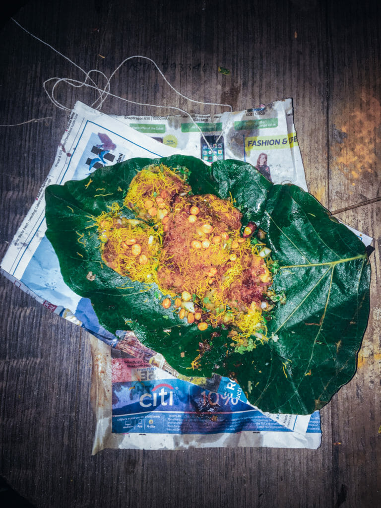 A pani puri snack on a large green leaf on some newspaper