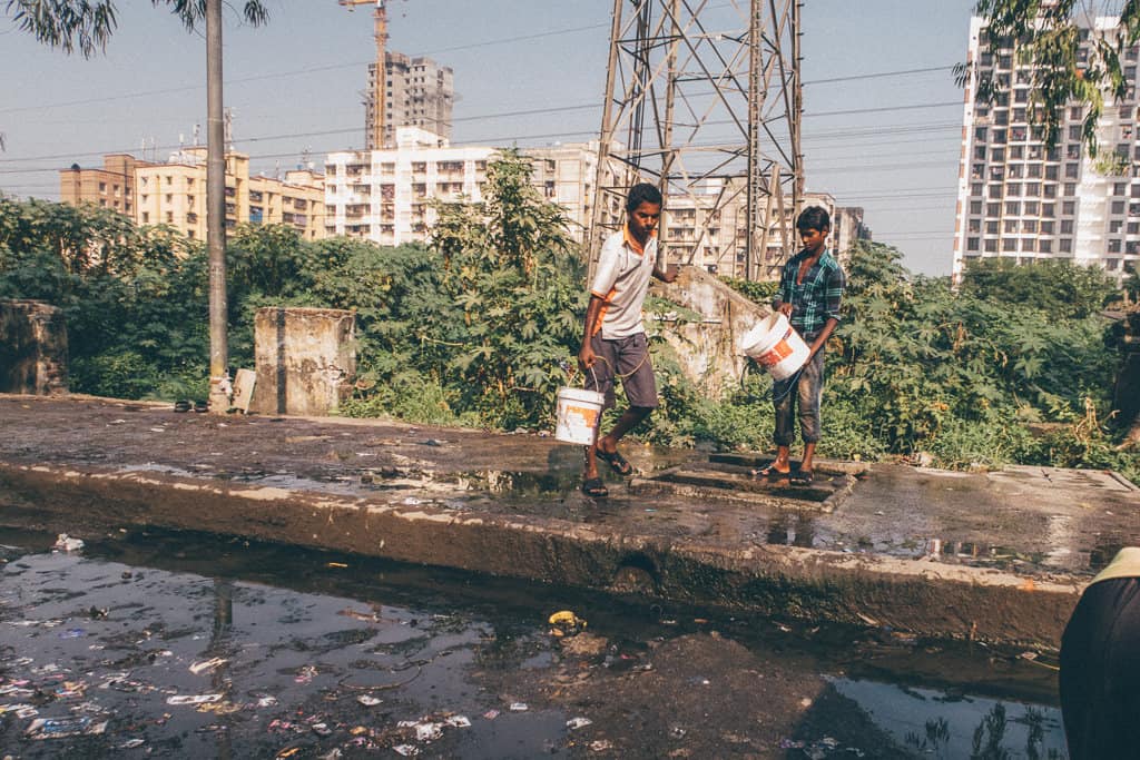 two men carry containers to collect water in a pothole-ridden road in Mumbai