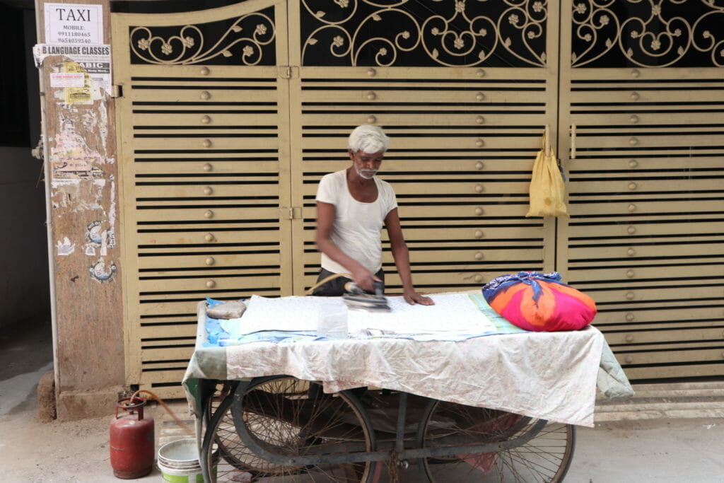 Photo of Yaseen ironing clothes at his cart, with the iron being heated through a connection to an LPG cylinder by his side