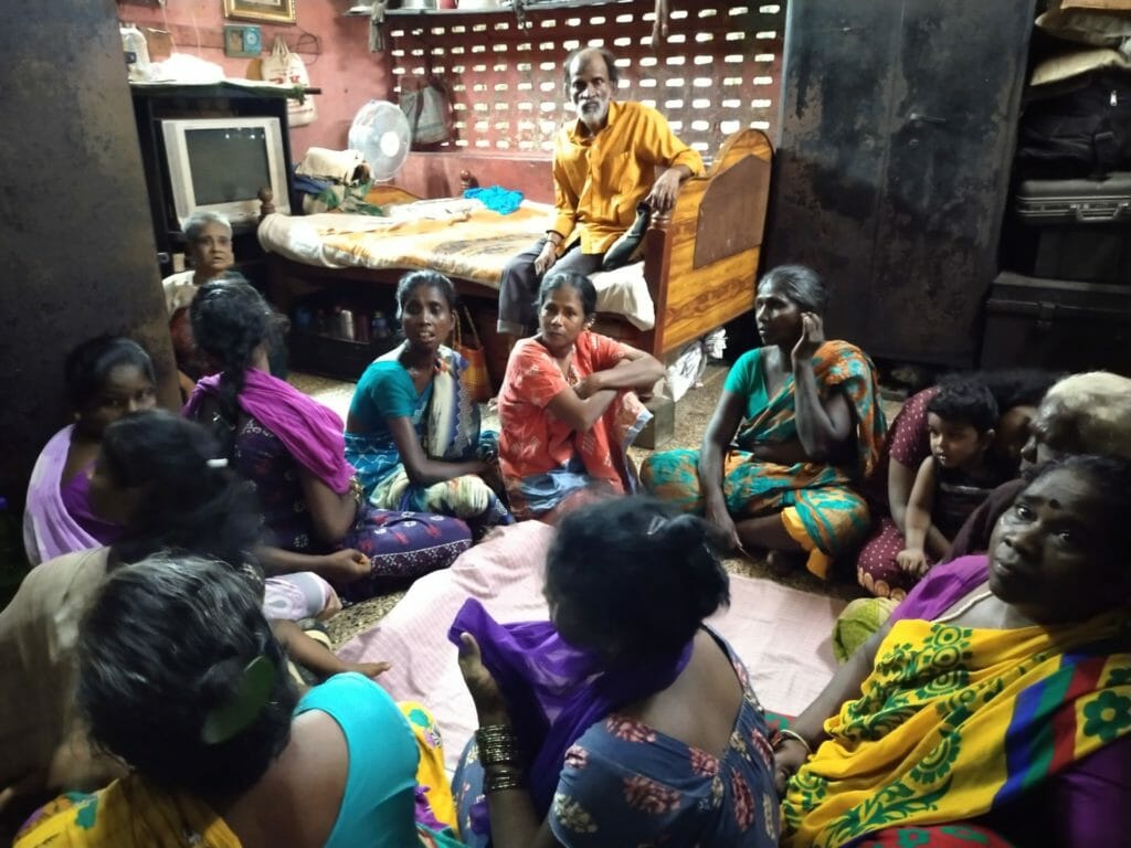 A group of women sitting in a room which is home to eight families
