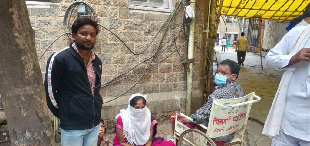 Deepak Khilare sitting in a wheelchair, he is wearing a surgical mask. Beside him is his wife, her face is covered with a scarf. Their son is sitting next to her and beside him is Kishore Khilare looking at the camera. The picture is shot inside KEM hospital.