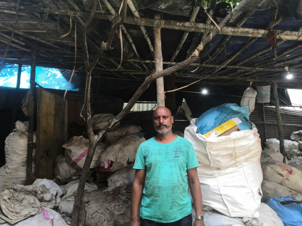 A man in a turqoise t-shirt standing in front of filled plastic sacks