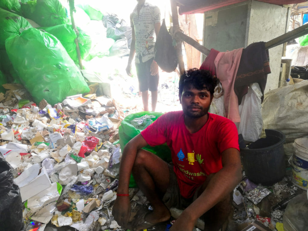 A man in a red shirt sitting besides a hill of waste paper, including disposable cups and tissues