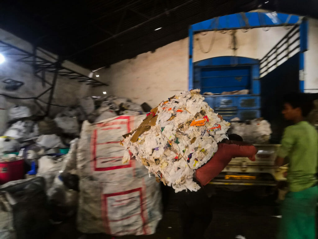 A man lifting a heavy bundle of paper waste into an open truck at the dry waste segregation centre