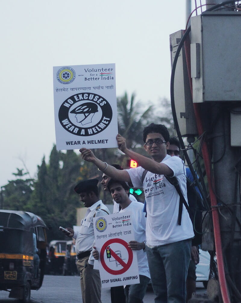 Volunteers holding placards urging drivers to follow the traffic rules of respecting signals and wearing helmets
