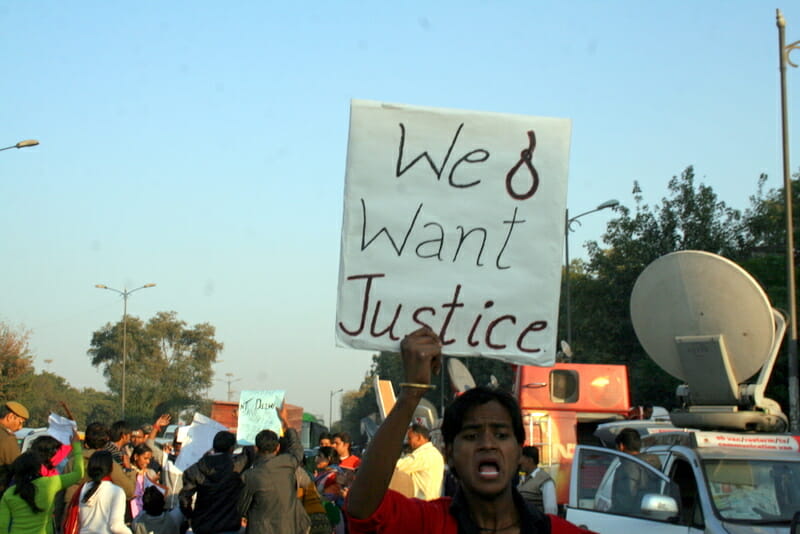 a transperson holds a sign at a protest for justice for a rape survivor 
