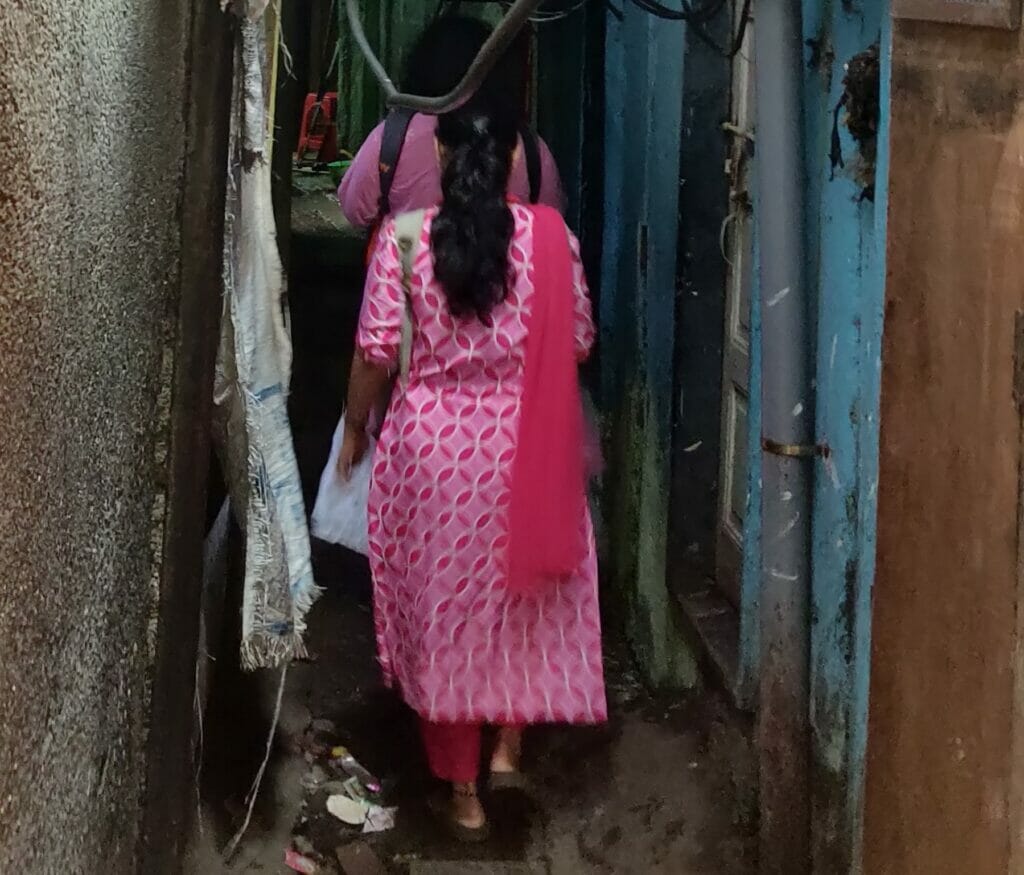Two women walking in narrow slum lanes.