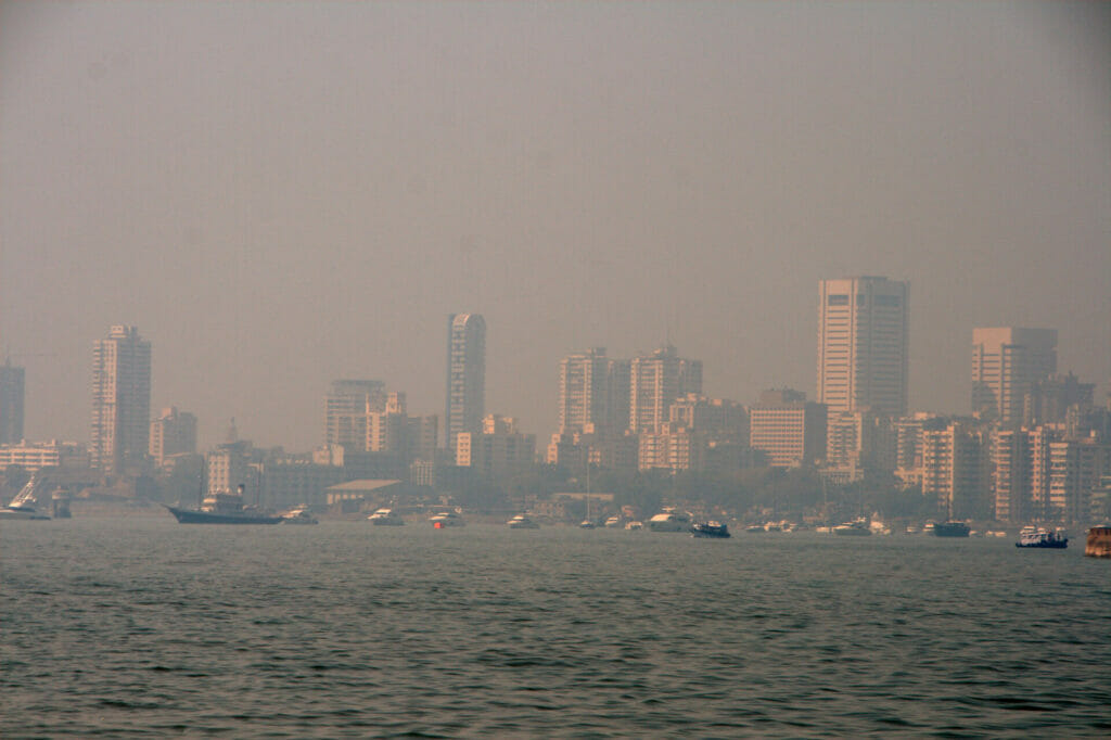 Smog over Mumbai's sea blanketing over tall buildings on the land.