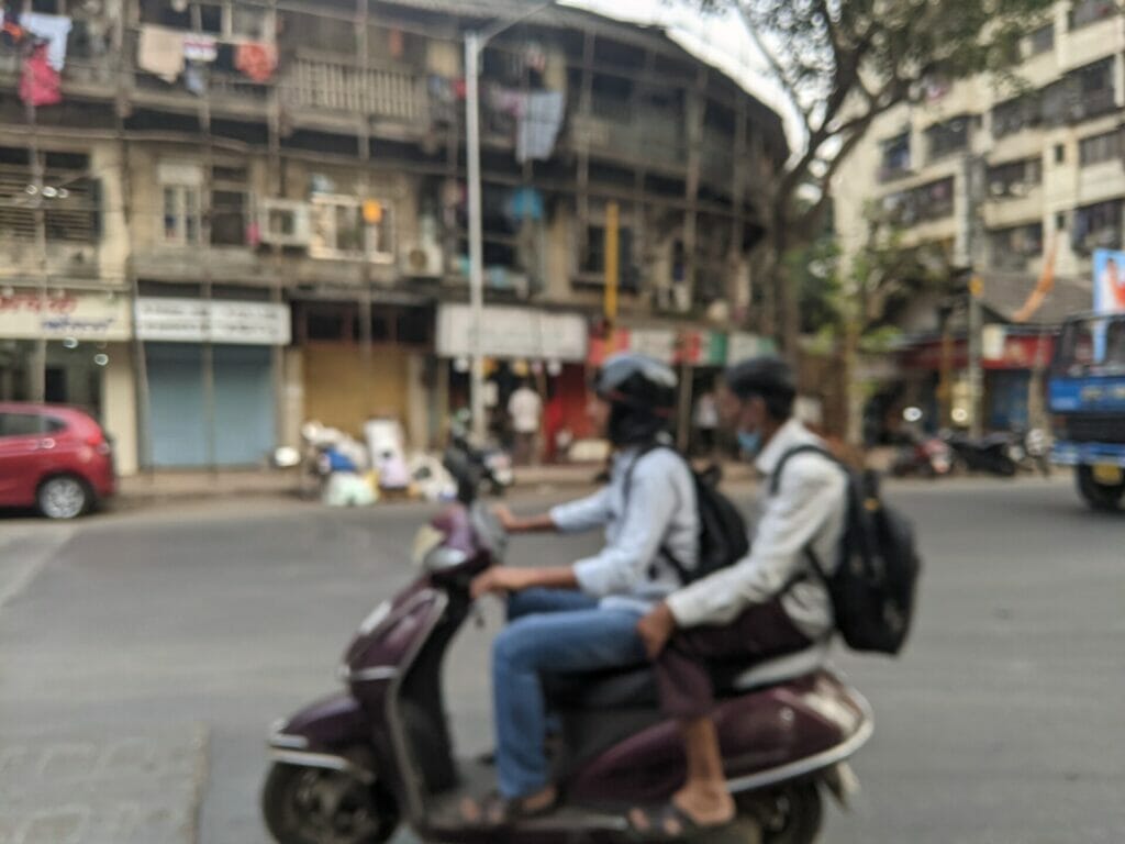 Two men on a two wheeler. The pillion is not wearing a helmet.