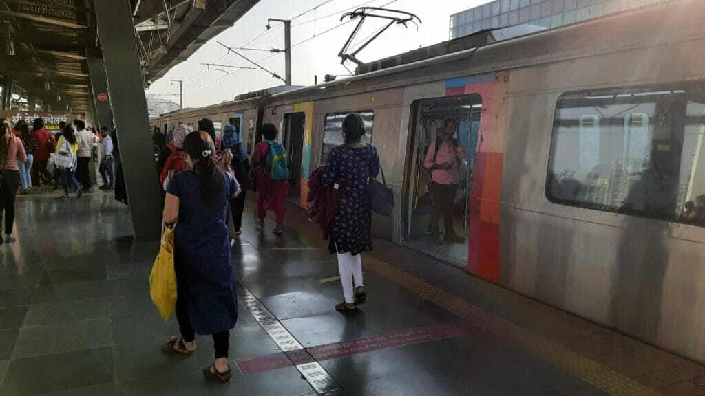 A metro train at a platform with people moving around on the station