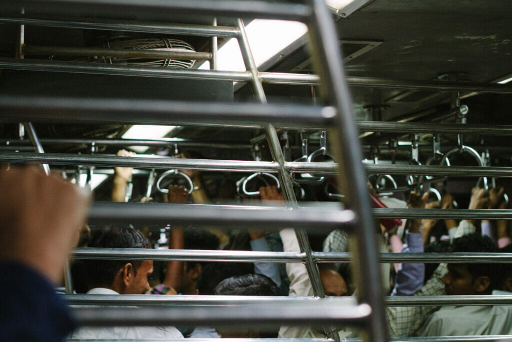 Men crowd in a train in Mumbai, with hands outstretched holding on to the handles