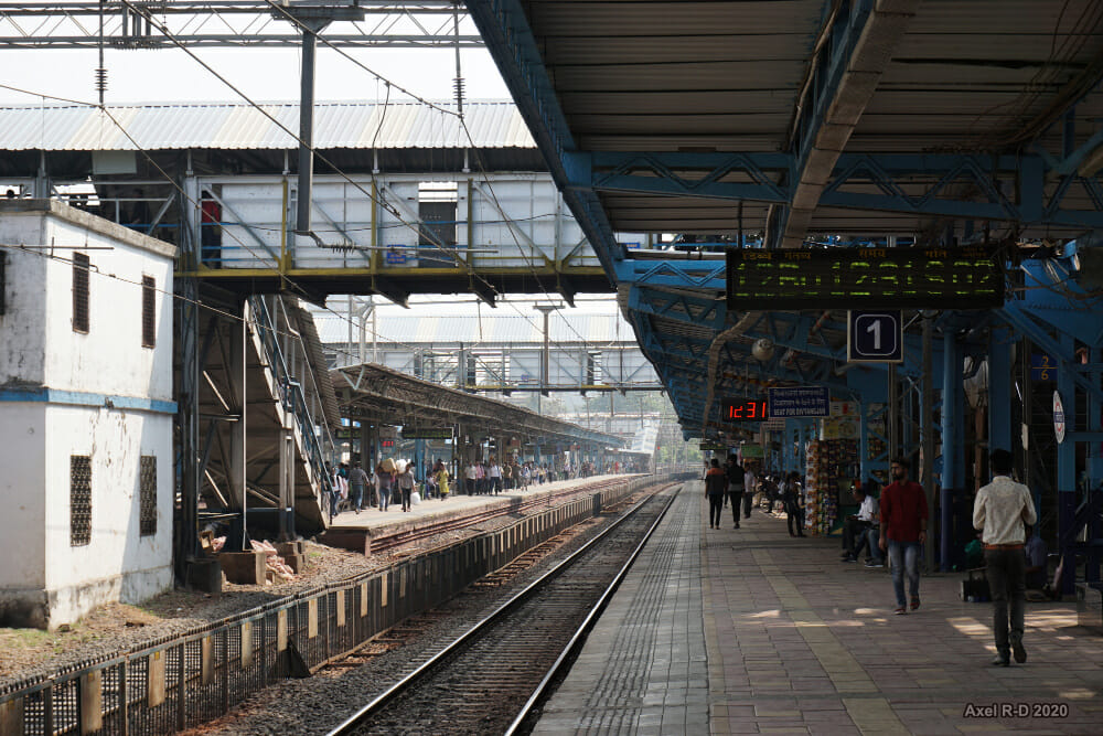 A train station platform in Mumbai, with people walking and waiting for the train