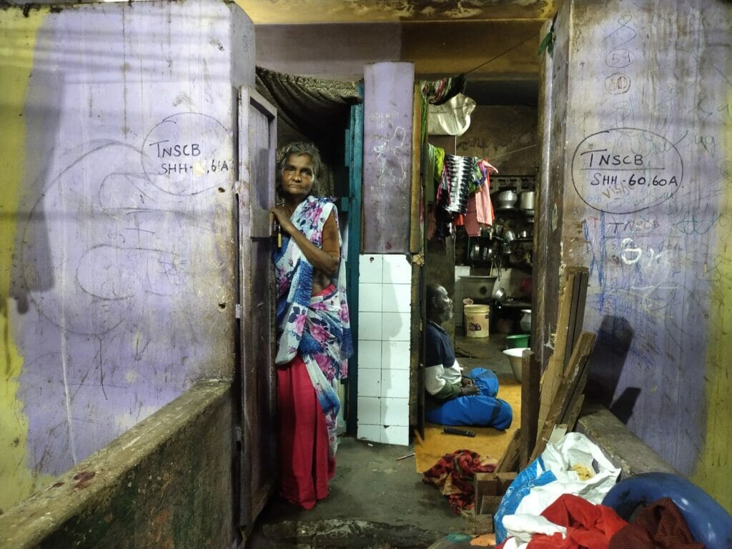 An old woman standing at the door of a single room house in Chennai.
