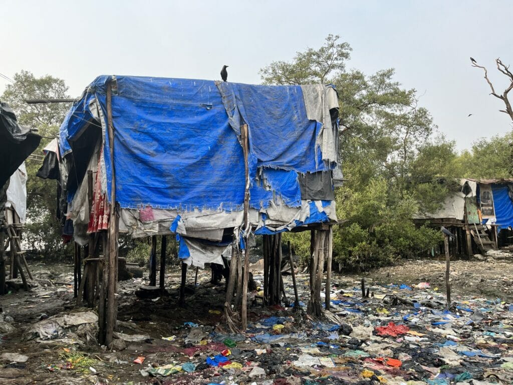 house on stilts with garbage strewn on the ground in a Mumbai slum