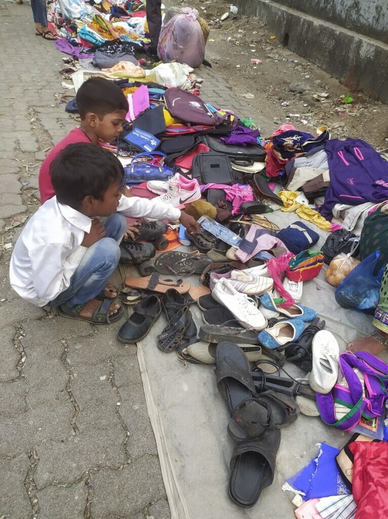 boys sitting next to shoes, gadgets and clothes on sale