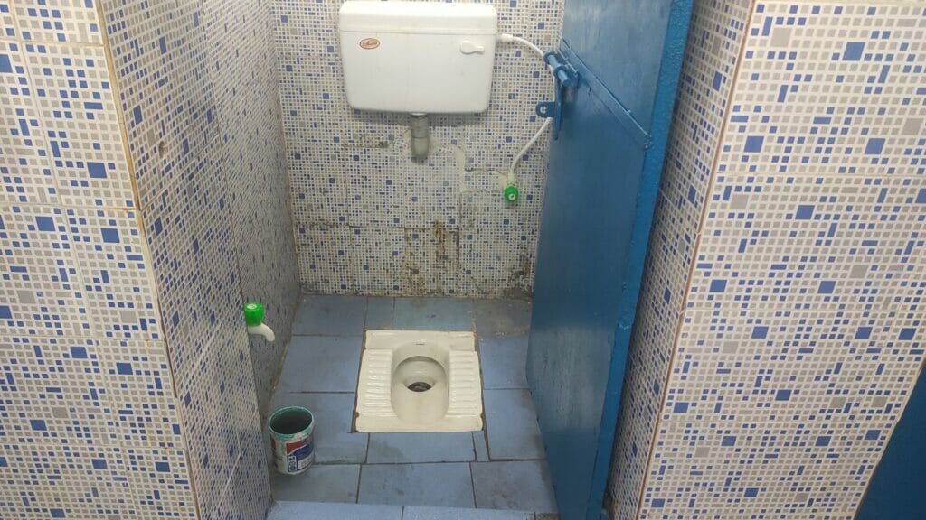 Indian toilet with a paint bucket filled with water
