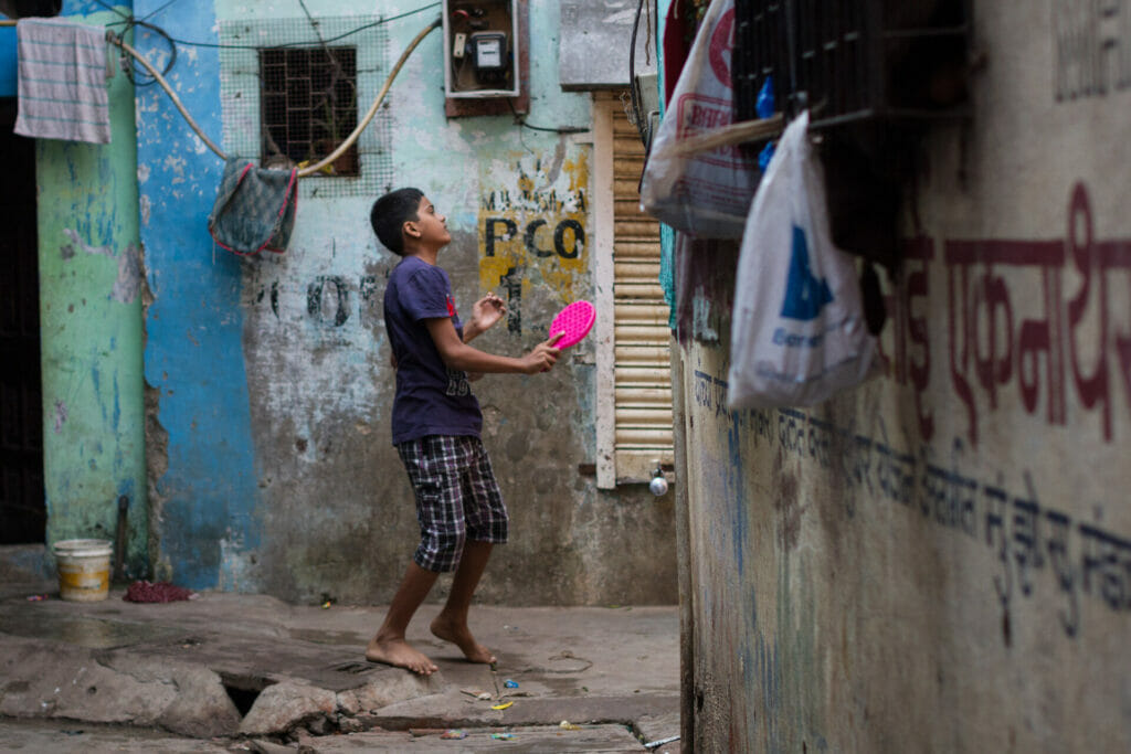 A boy playing paddle in the galli of a slum
