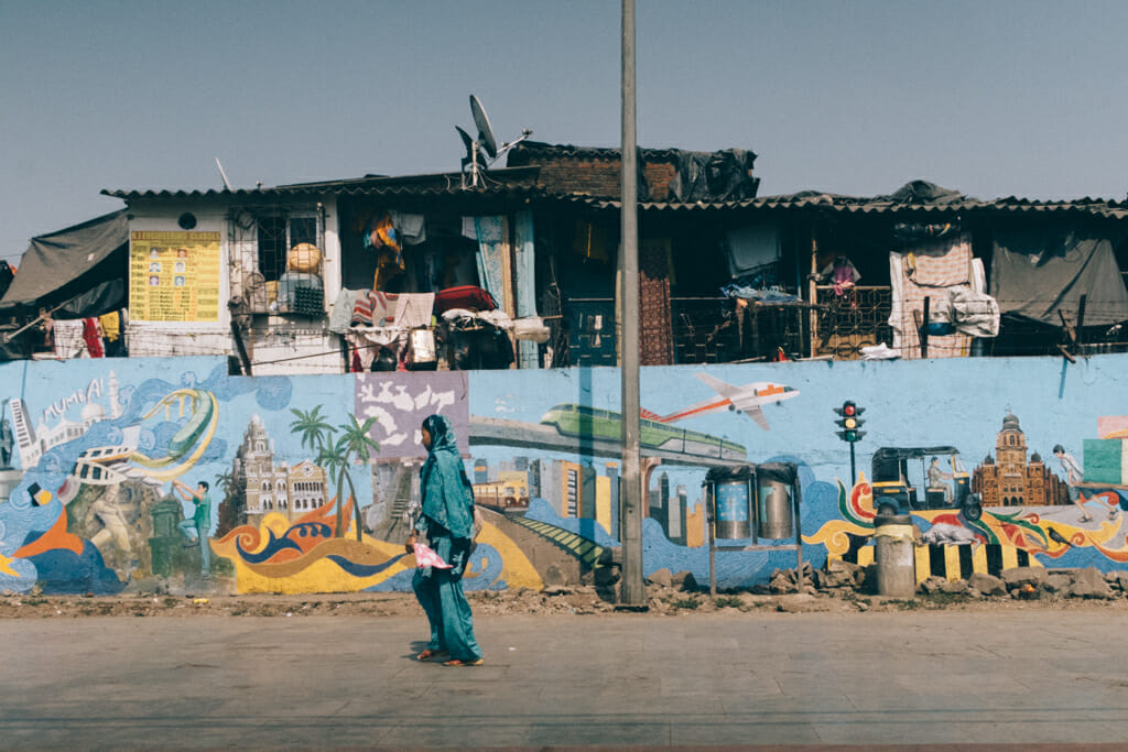 Lady walking across a painted wall in front of a slum