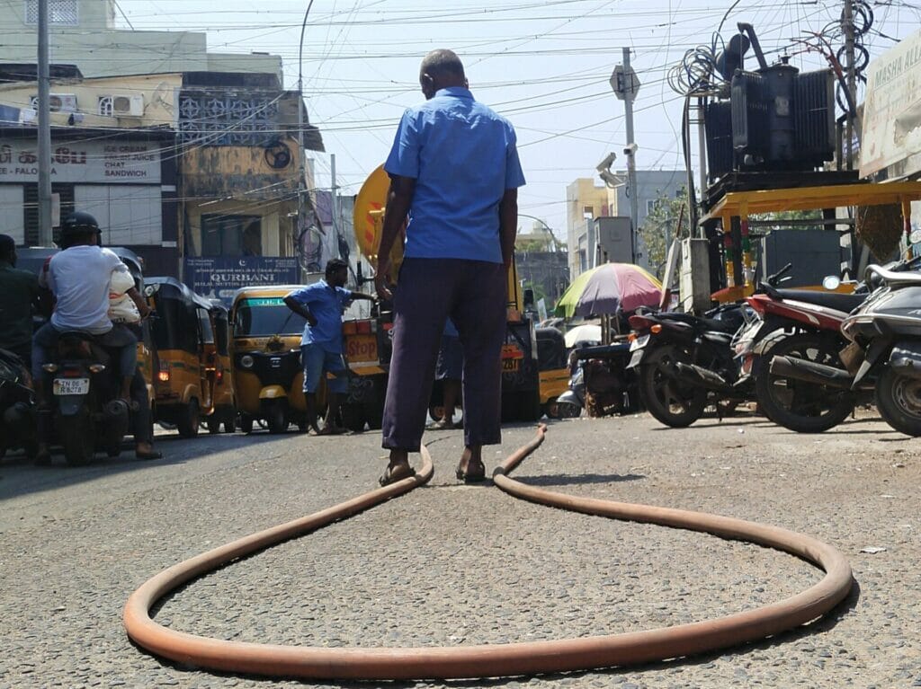A manual worker standing a guard to prevent the commuters from slipping on the road due to the spread out the hose. 
