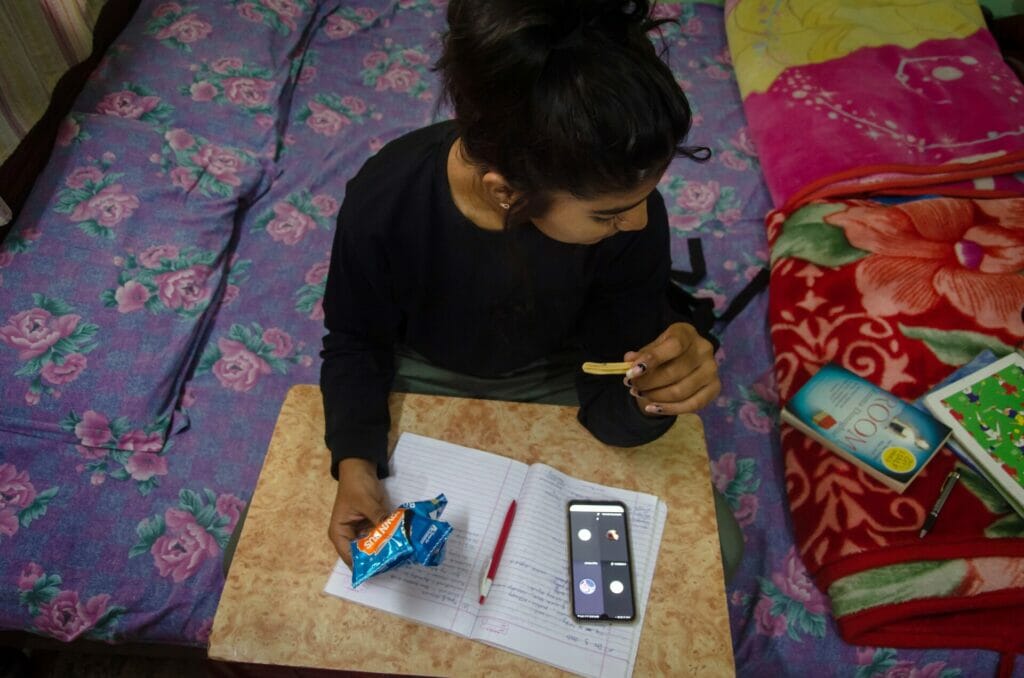 A girl studying at home, using her mobile phone while eating a snack
