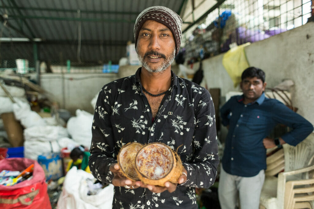 A waste worker in Bengaluru holds up two coconut shells.