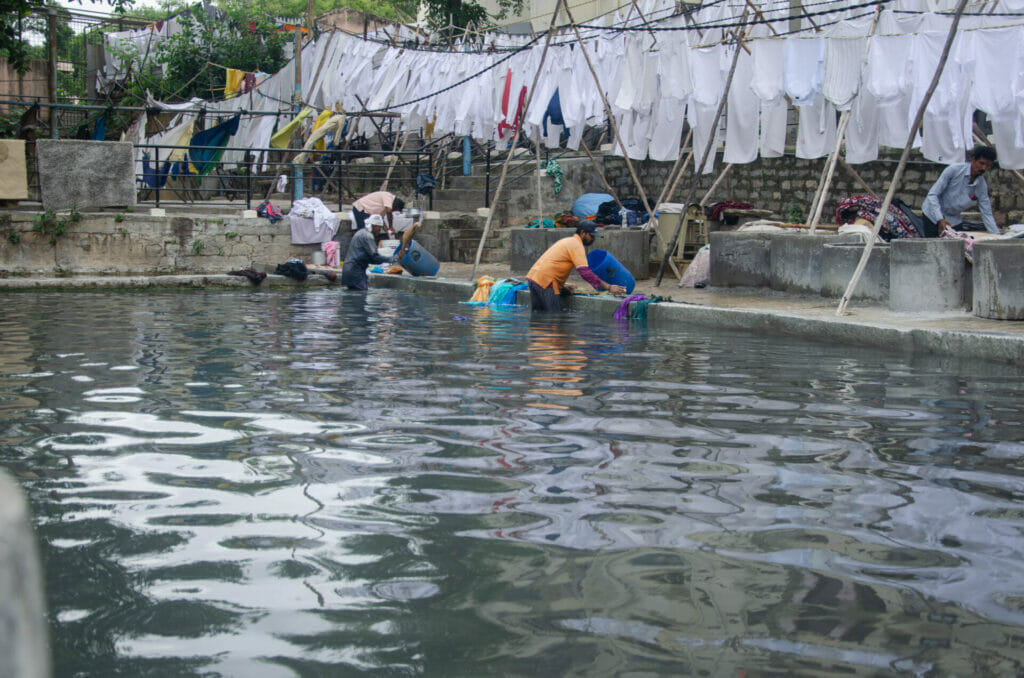 Dhobis in knee deep water washing clothes in the water hole of the dhobi ghat