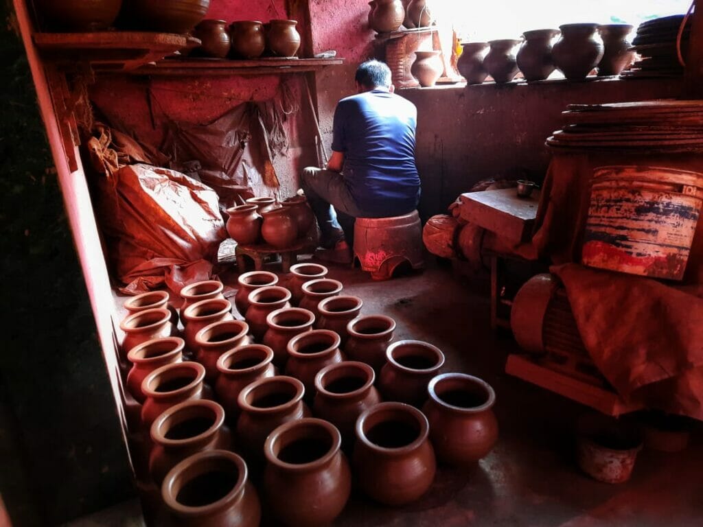 an artisan makes pots as others other pots are lined up for drying. 