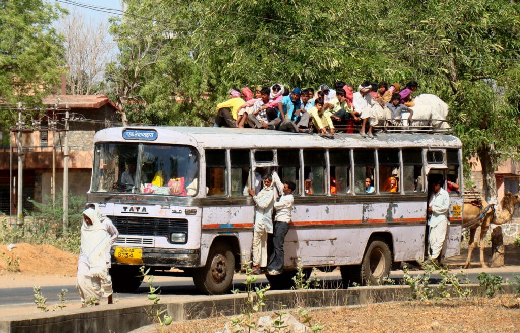 Travellers sit on the roof of a crowded bus.