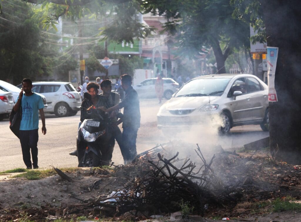 Garbage being burnt on the side of a road in Dehradun, while men stand right next to it.
