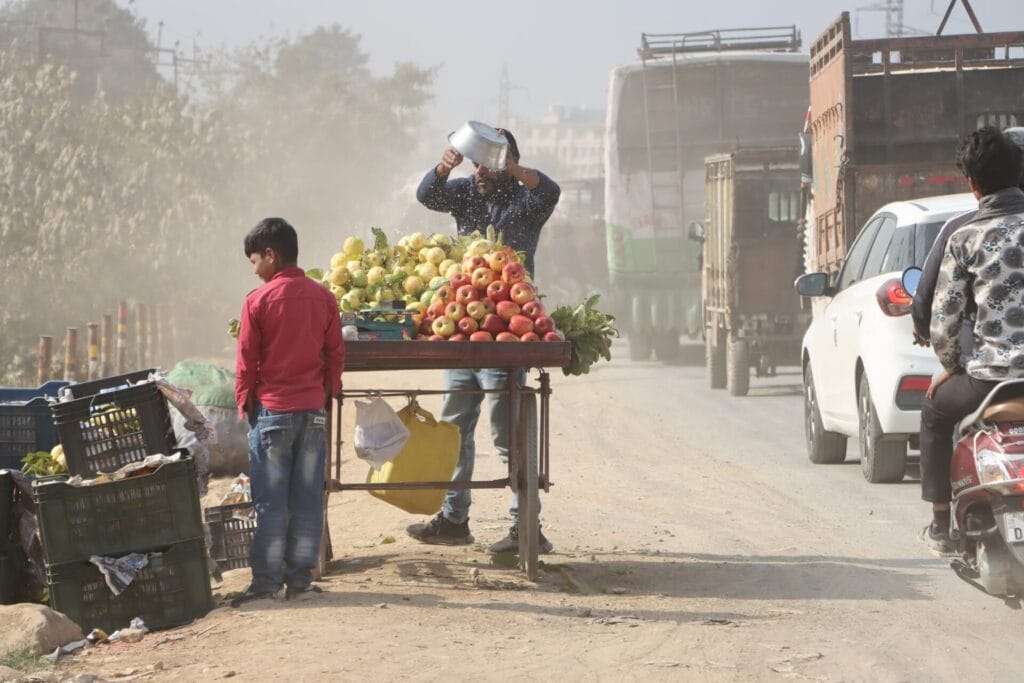 Street vendor and his son stand near their cart by the side of a polluted road.